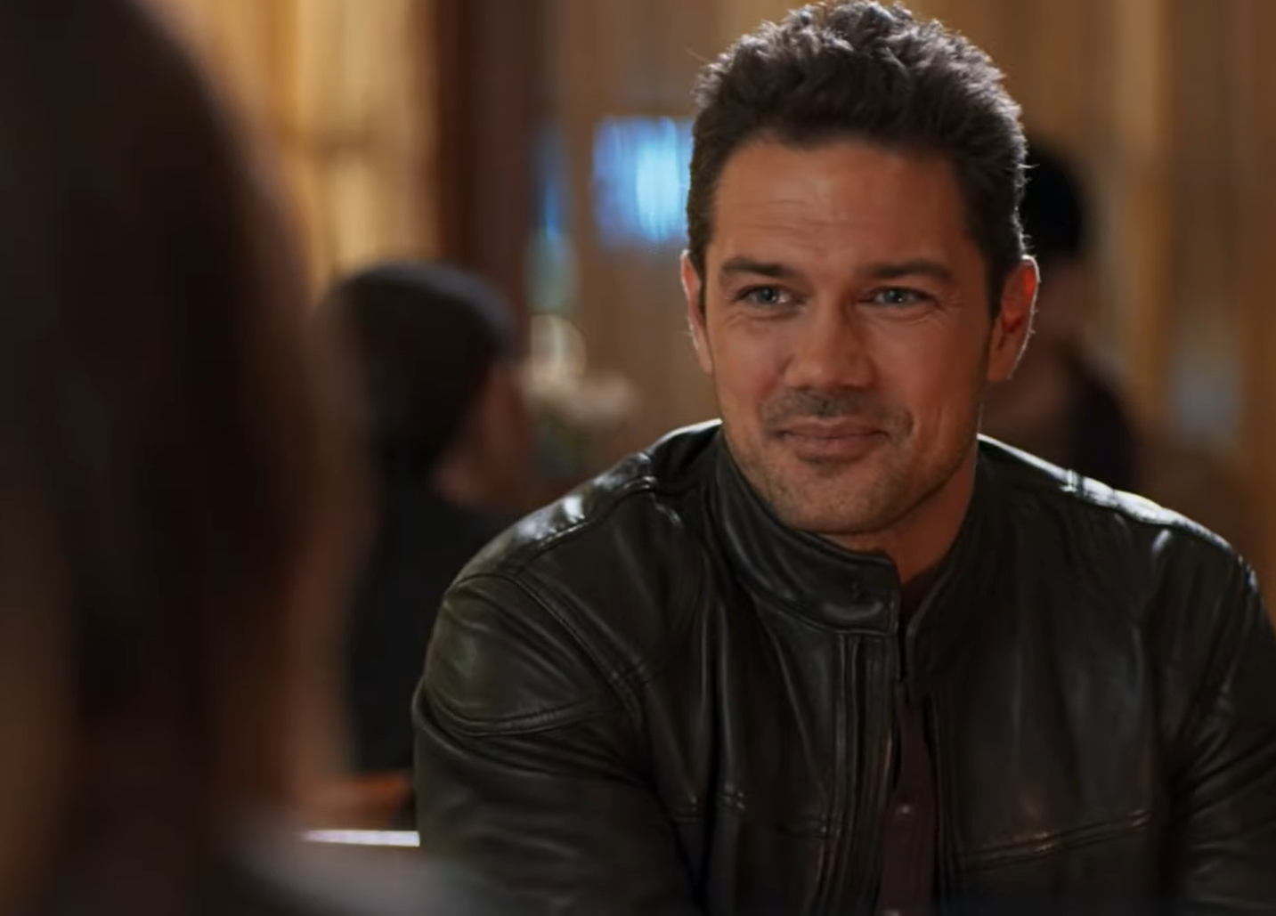Ryan Paevey in leather jacket sitting in front of the woman and smiling