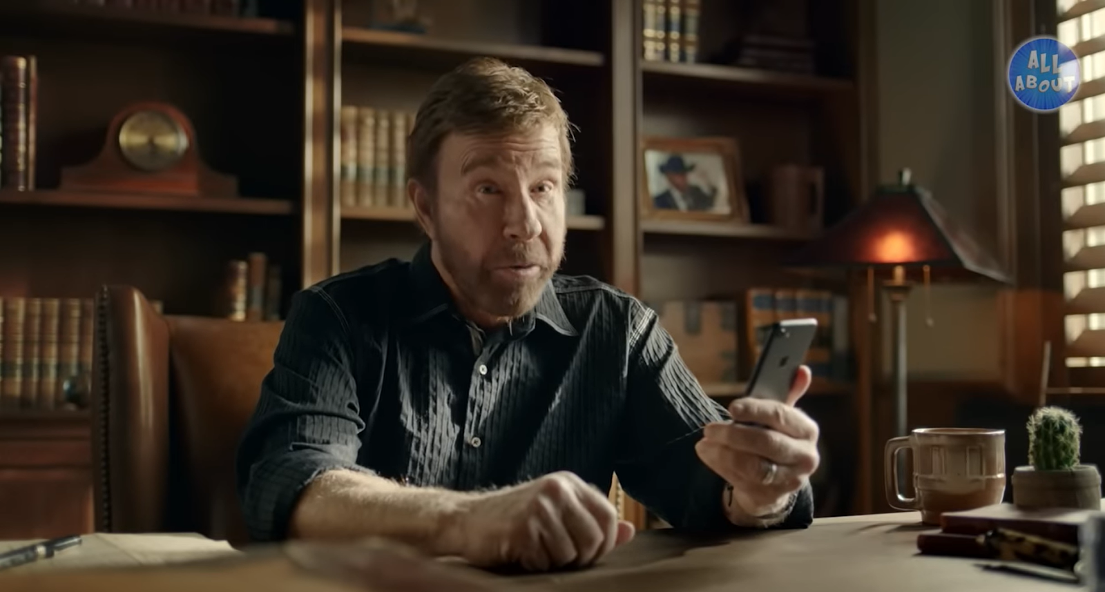 Chuck Norris sitting at the table holding the phone in his left hand and looking forward