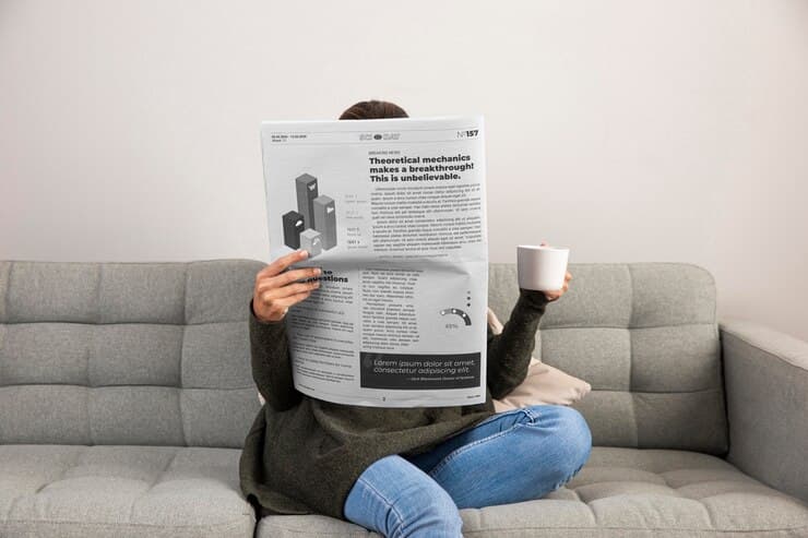 Woman Sitting on Couch with Cup and Newspapers
